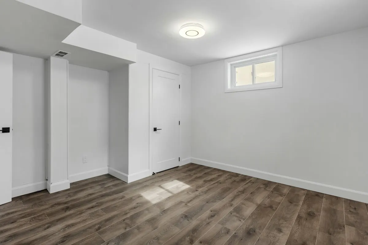 Finished basement room with fresh white walls and wood-look flooring